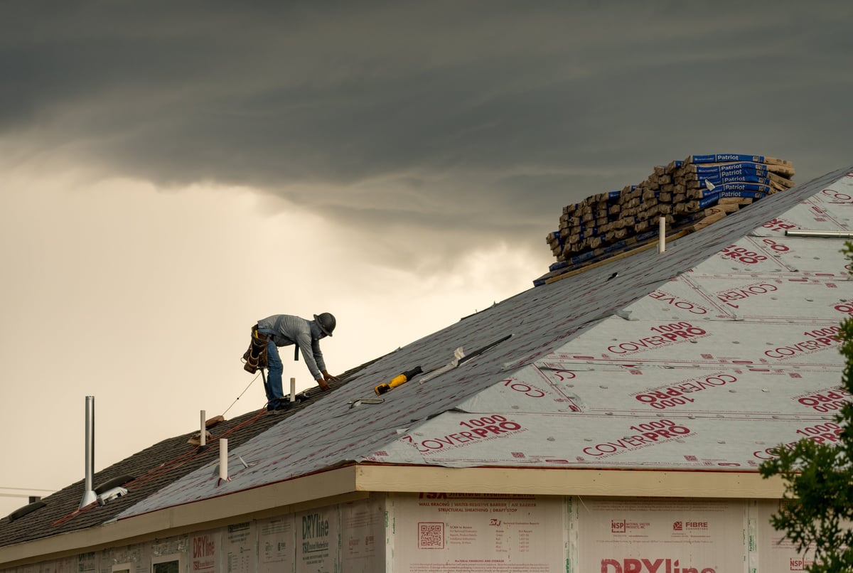 Roofer installing shingles during severe North Texas weather
